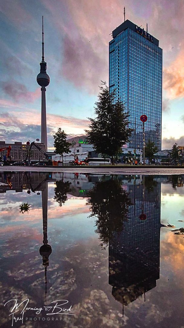 Sunset at Alexanderplatz with a puddle and the reflection of TV tower and parkin hotel