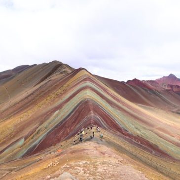 Panoramic view of Rainbow Mountain (Vinicunca) with colorful stripes, hikers on the trail, and Andes peaks in the background, Peru.